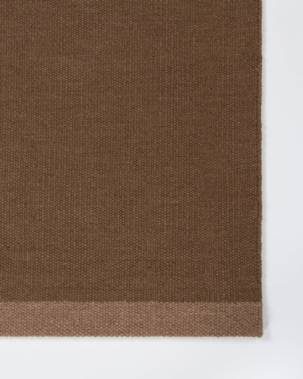 Baya Carla NZ wool floor mat in Cocoa, close view of the woven texture and the lighter brown end band.