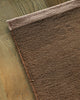 Baya Carla NZ wool floor mat in Cocoa, folded corner showing the weave and underside on a wood floor.