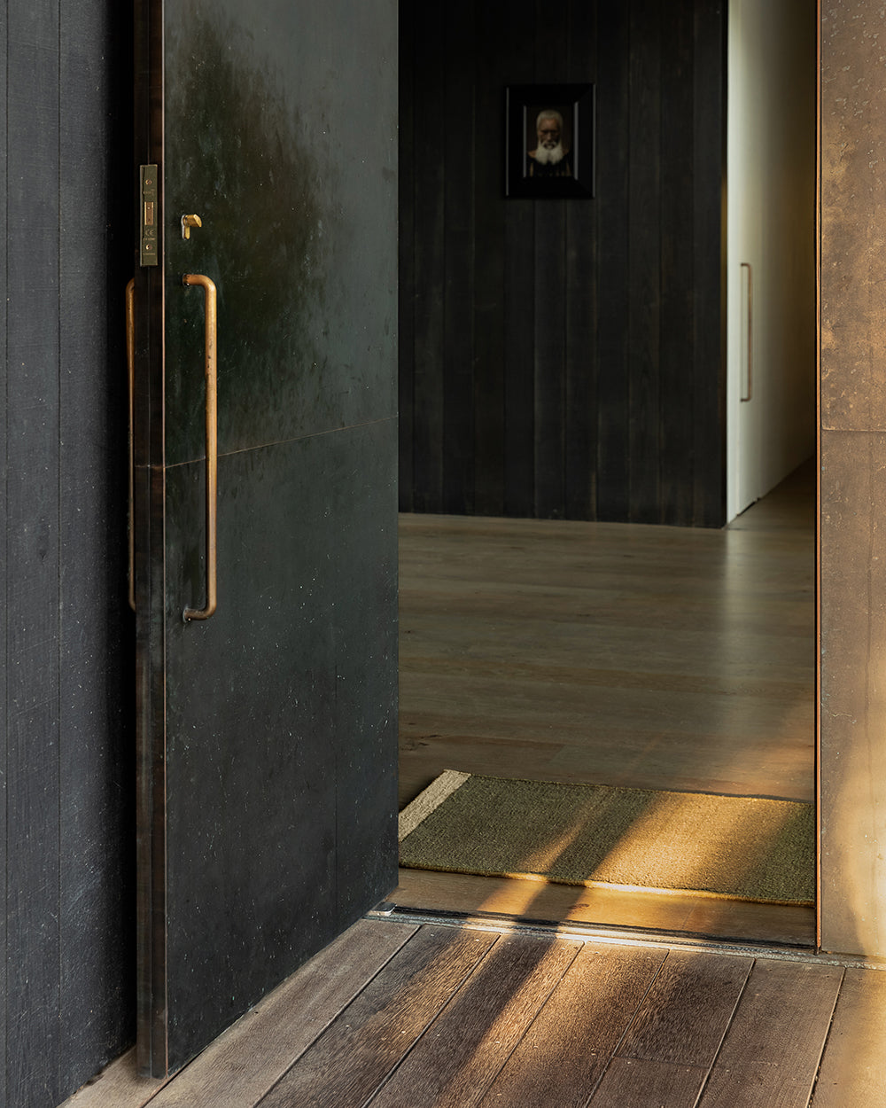 Baya Carla NZ wool floor mat in Military, styled at a dark entranceway beside an open door.