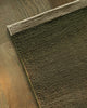 Baya Carla NZ wool floor mat in Military, folded corner showing the weave and underside on a wood floor.