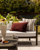 Baya Clipper recycled PET outdoor lumbar cushion in Claret styled on an outdoor sofa, wide view
