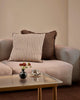 Baya Dover Chocolate cushion styled on a grey sofa alongside a striped cushion, close view with a vase of flowers on the coffee table