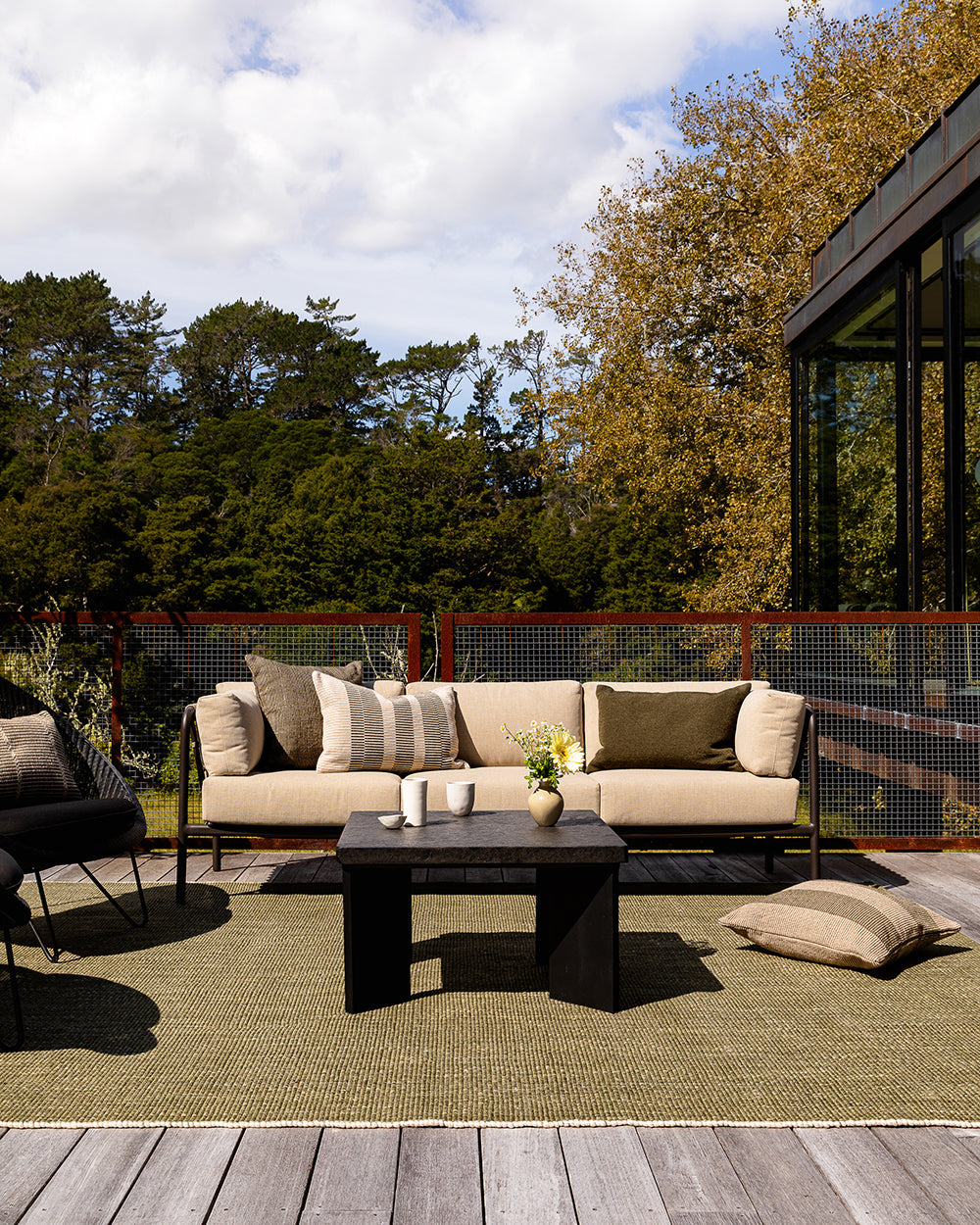 Baya Dune outdoor cushion in Mangrove styled on an outdoor deck setting with a sofa and armchair