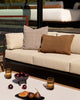 Baya Dune outdoor cushion in Tobacco styled on an outdoor sofa beside a solid rust-brown lumbar cushion, with a styled coffee table setting