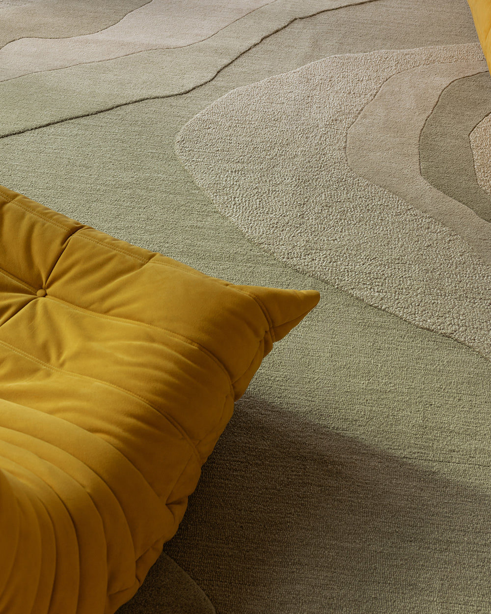 Baya Edgewater NZ wool floor rug in Pistachio, rectangle, close view of the wave pattern beside a mustard lounge chair.