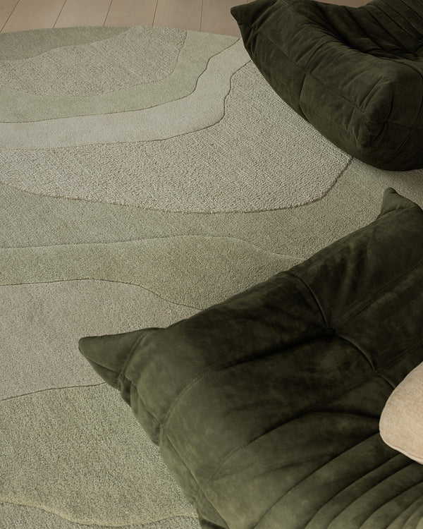 Baya Edgewater NZ wool floor rug in Pistachio, round, close view of the wave pattern beside dark green velvet lounge chairs.