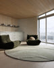 Baya Edgewater NZ wool floor rug in Pistachio, round, styled in a bright room with two dark green lounge chairs and a window.