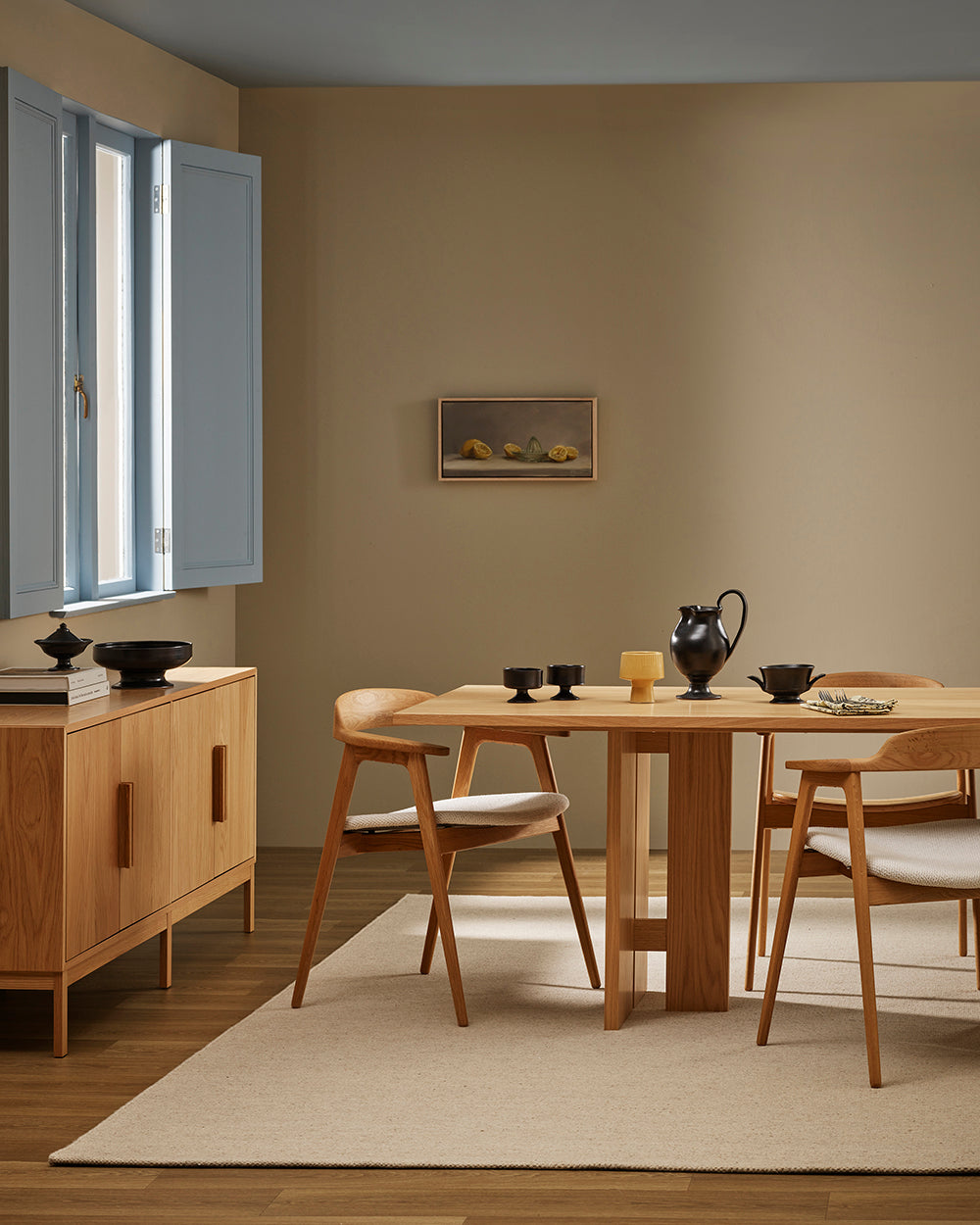 Baya Fairmont NZ Wool Floor Rug in Limestone, under a dining table beside a sideboard, with blue window shutters