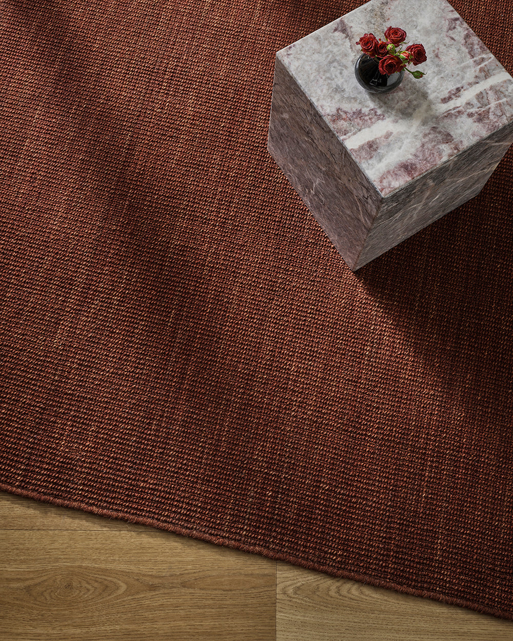 Overhead styling shot of the Baya Linden Floor Rug in Brick beneath a marble side table with a vase of red roses.