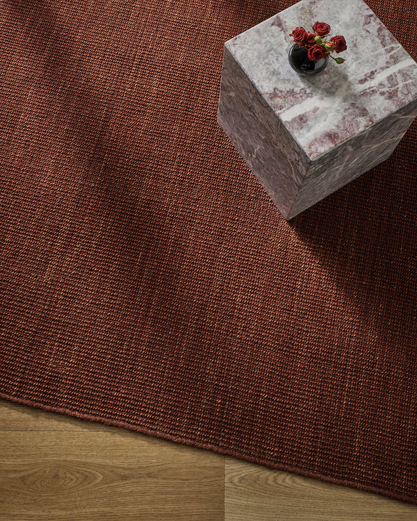 Overhead styling shot of the Baya Linden Floor Rug in Brick beneath a marble side table with a vase of red roses.