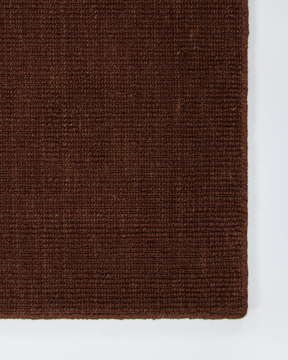 Close-up of the Baya Linden Floor Rug in Brick showing its dense flatweave texture and finished fringed edge in an earthy red-brown wool.