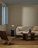 The Baya Linden Floor Rug in Ironbark styled in a living room with a beige sofa, leather armchair and round coffee table, showing its earthy brown tone.