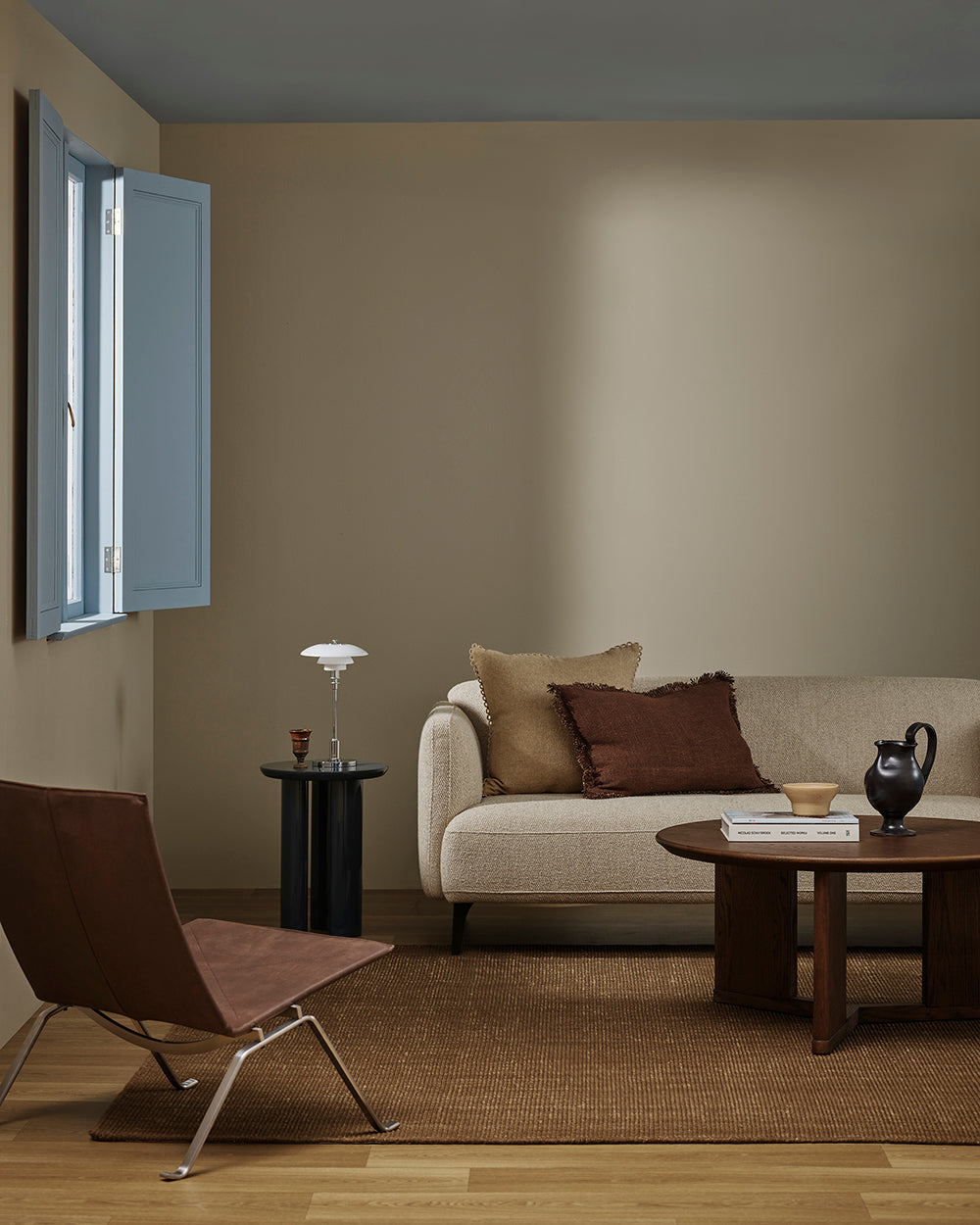 A second view of the Baya Linden Floor Rug in Ironbark styled in the same living room, with a beige sofa, leather armchair and round coffee table.