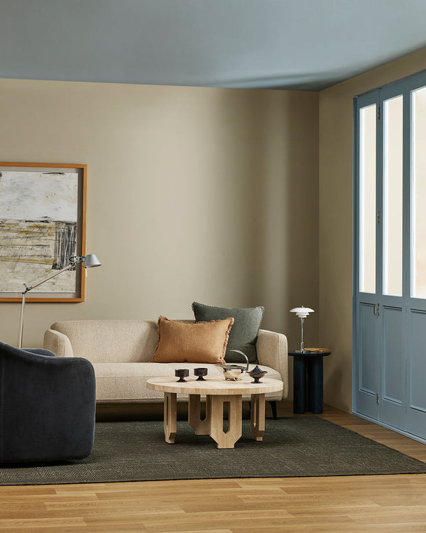 The Baya Linden Floor Rug in Petrol styled in a living room with a cream sofa, dark armchair and blue-shuttered doors, showing its deep green-toned wool.