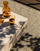 Baya Ormond outdoor rug in Mineral, styled on a deck under a pale stone table with an amber glass carafe and tumblers.