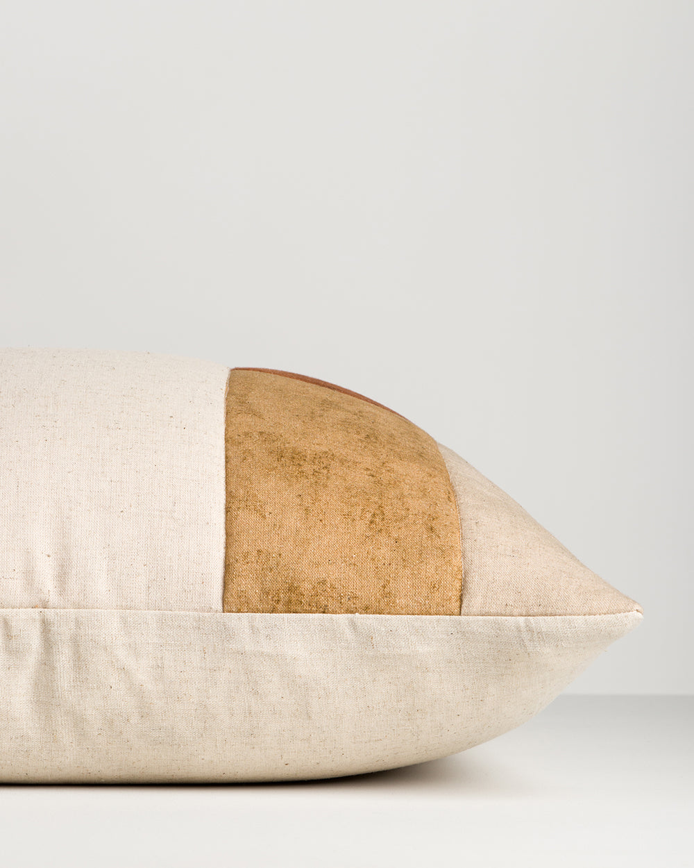 Baya Piazza Cushion in Multi, side profile lying flat, showing the ochre panel and natural linen back.