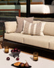 Baya Solar Outdoor Lumbar Cushion in Chocolate, styled on an outdoor sofa beside a plain cushion, with a table setting nearby.
