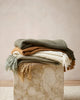 Pile of soft, earthy coloured throw blankets on a marble plinth, by Baya nz