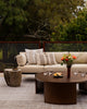 Baya Tide Outdoor Cushion in Almond styled on an outdoor sofa in soft evening light, with flowers and fruit.