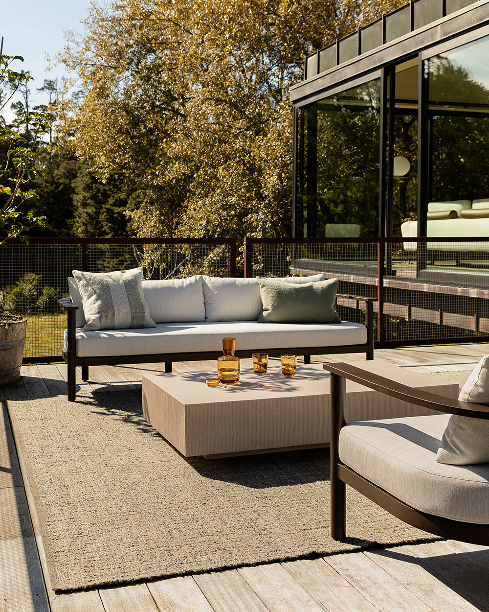 Baya Tide Outdoor Cushion in Eucalyptus styled on an outdoor sofa on a deck, with a lounge chair and coffee table.