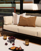 Baya Tide Outdoor Cushion in Tobacco styled on an outdoor sofa with a solid brown Baya cushion.