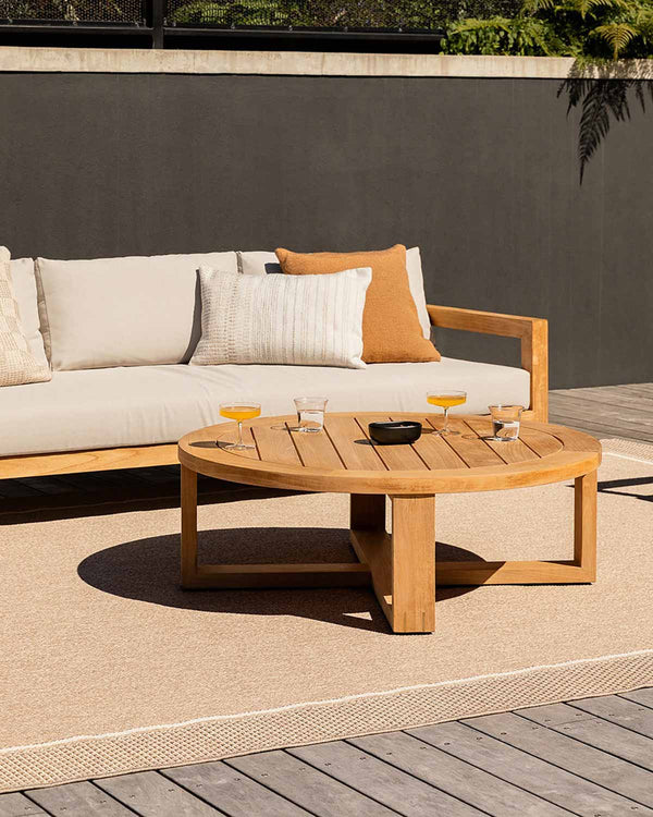 A neutral toned outdoor rug by Baya NZ, under a couch and table with cocktails on it on a deck. 