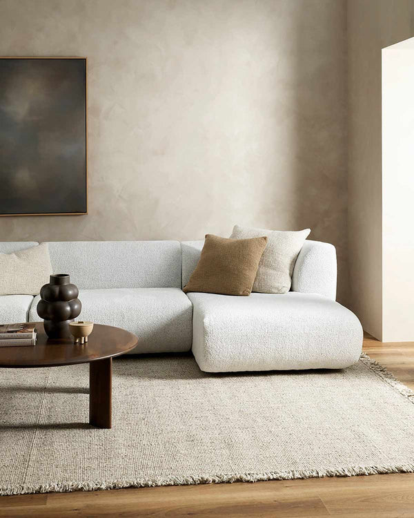 A modern living room with a couch, coffee table, and neutral toned, fringed rug by Baya NZ