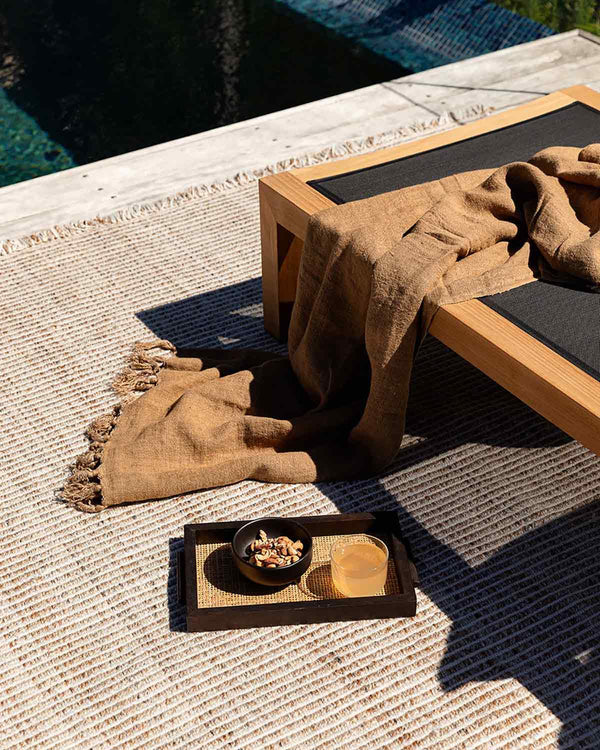 The teak-brown Rhodes outdoor rug by Baya NZ, seen outside in the sun under stylish outdoor  furniture
