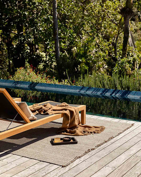 The Rhodes Teak Outdoor rug by Baya, seen under a lounger on the deck of a contemporary home
