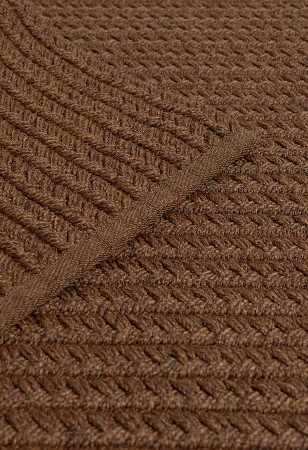 By Carmont Aman floor rug in Coffee, diagonal view showing the braided weave with the edge binding crossing it.