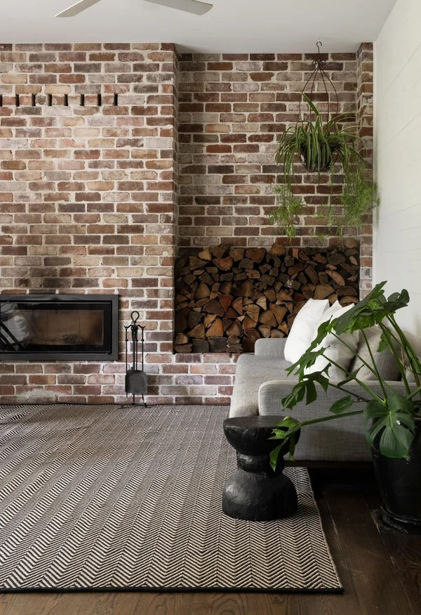 By Carmont Bhumi Floor Rug in Seraphic styled in a living room with a brick fireplace