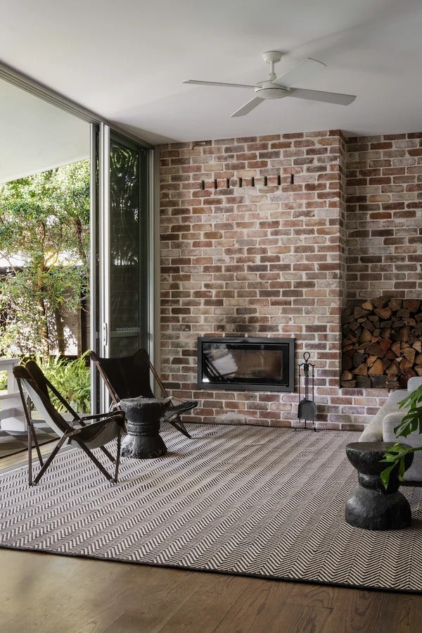 By Carmont Bhumi Floor Rug in Umber styled in an indoor-outdoor living room with a brick fireplace