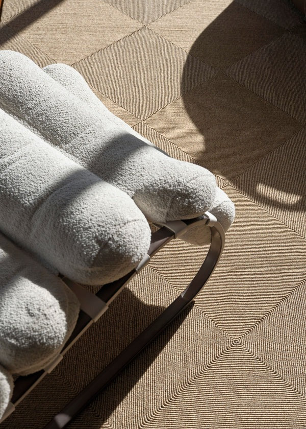By Carmont Capella floor rug in Natural underfoot beside a cream bouclé lounge chair in natural light