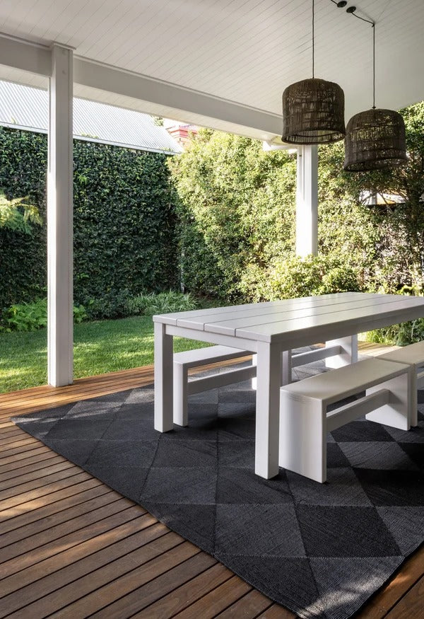 By Carmont Capella floor rug in Sable on an outdoor deck under a dining table and bench setting