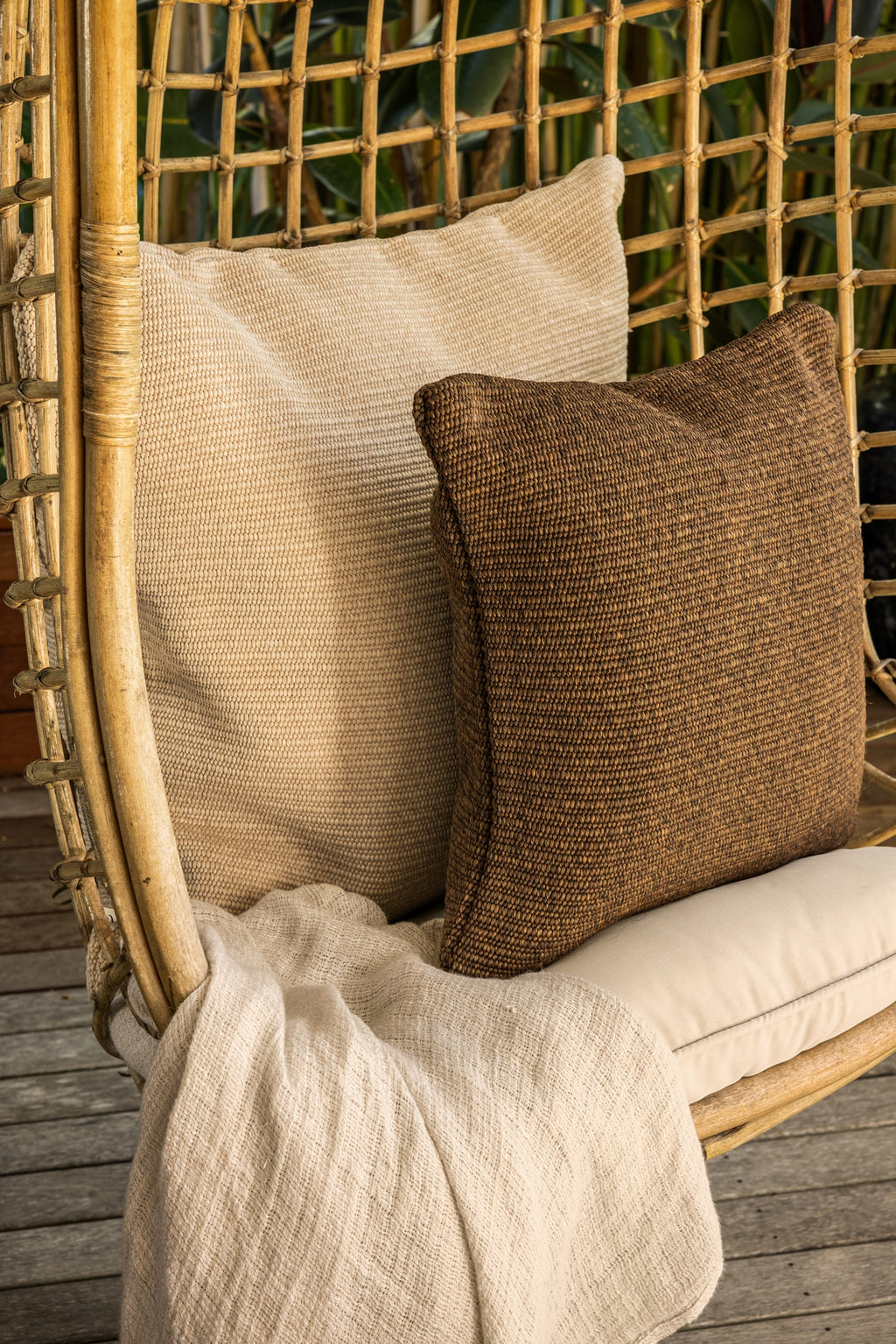 By Carmont Huxley cushion cover in Cameo on a hanging chair, behind a brown cushion with a pale throw