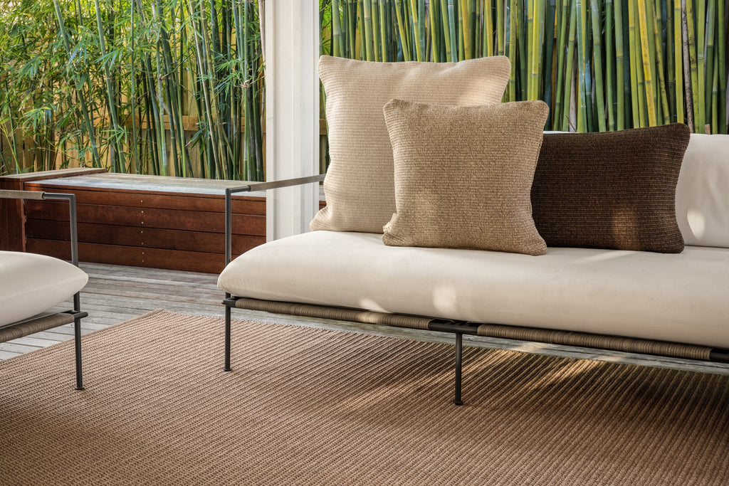 By Carmont Huxley cushion cover in Cameo on an outdoor sofa, behind a tan cushion and beside a dark brown one
