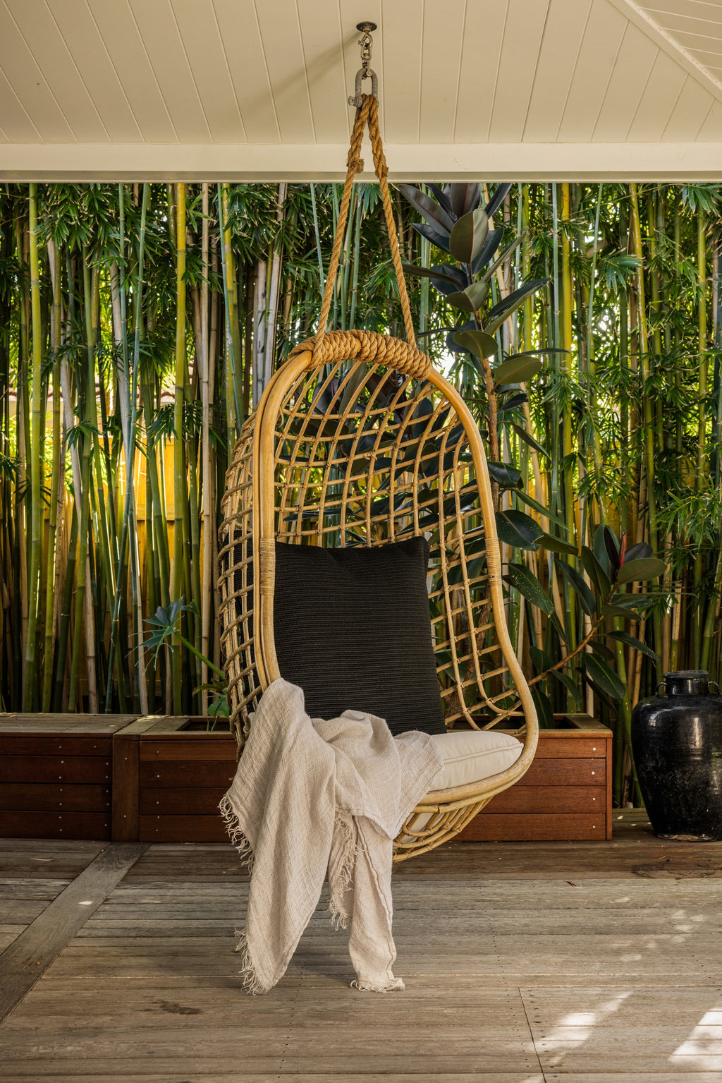 By Carmont Huxley cushion cover in Sable on a chair hanging from the ceiling of a covered deck