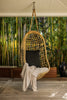 By Carmont Huxley cushion cover in Sable on a chair hanging from the ceiling of a covered deck