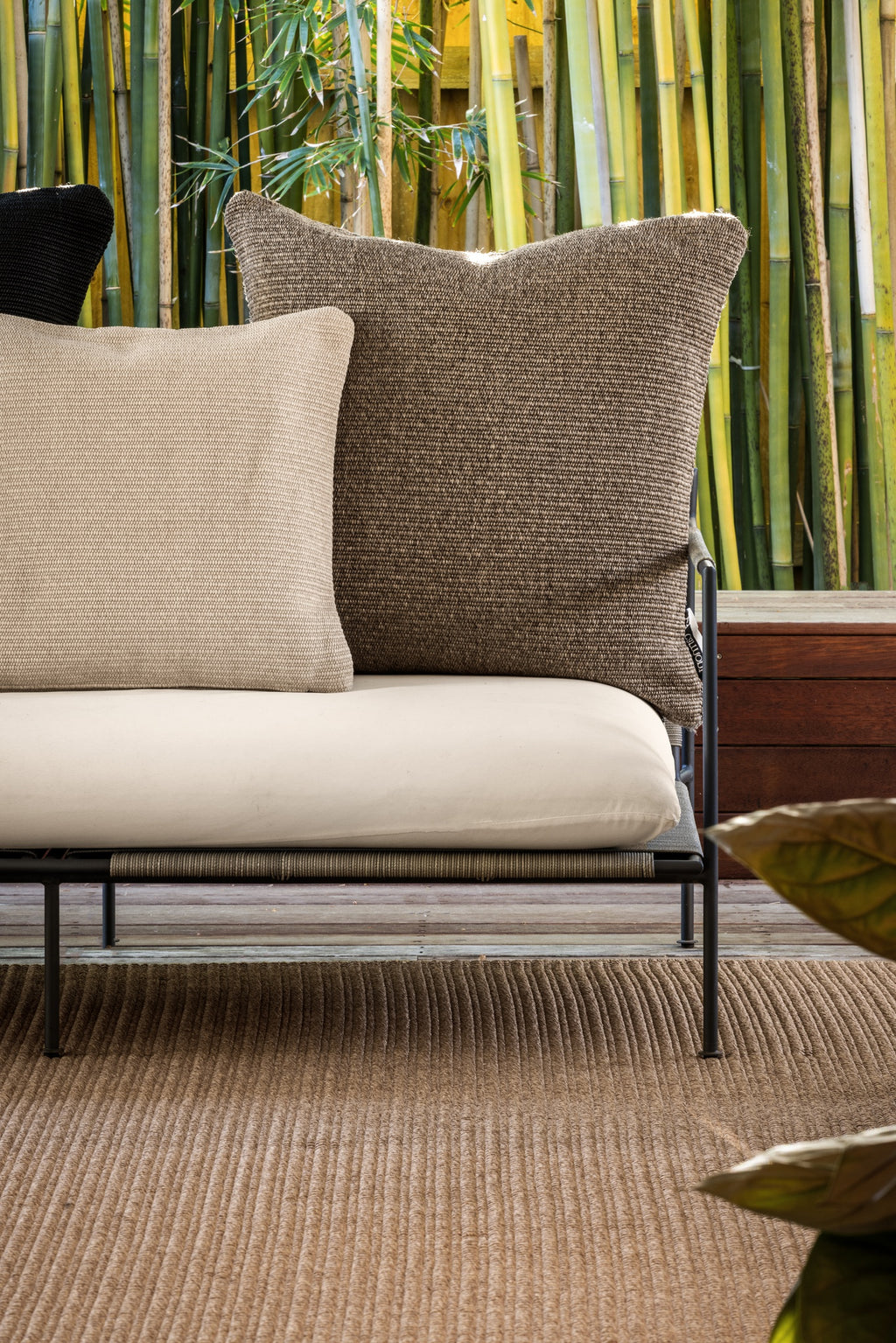 By Carmont Huxley cushion cover in Topaz at the end of an outdoor sofa, behind a smaller pale cushion