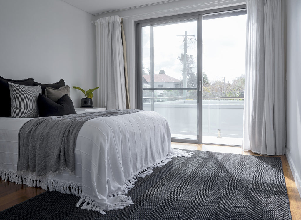 By Carmont Sapphire floor rug in Ambrosia, styled at the foot of the bed in a bedroom.