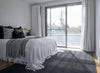 By Carmont Sapphire floor rug in Ambrosia, styled at the foot of the bed in a bedroom.