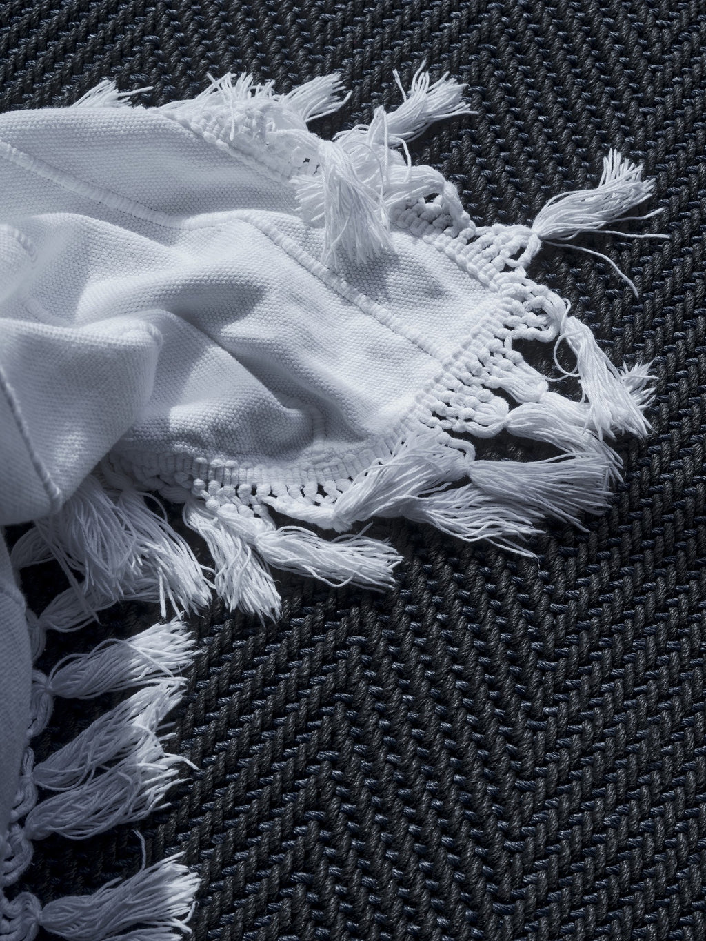 By Carmont Sapphire floor rug in Ambrosia, close view of the weave with a fringed throw laid over it.