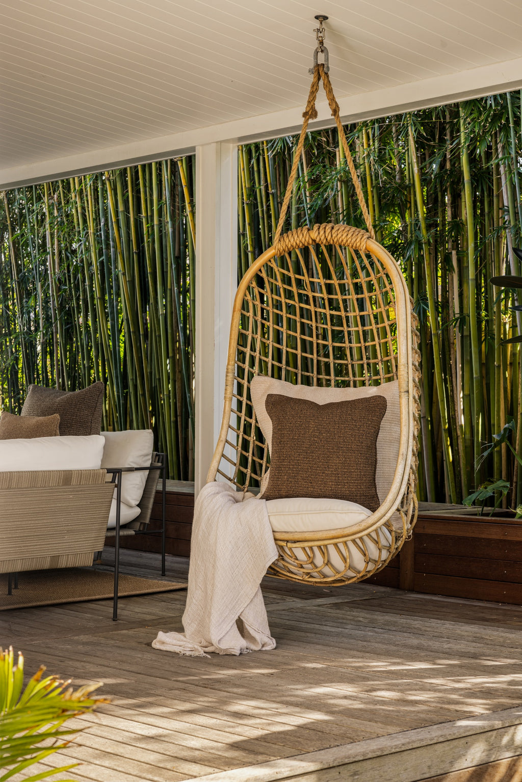By Carmont Wren cushion cover in Topaz on a hanging chair, wide view of a covered deck and outdoor sofa