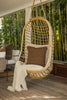 By Carmont Wren cushion cover in Topaz on a hanging chair, angled view with an outdoor sofa behind