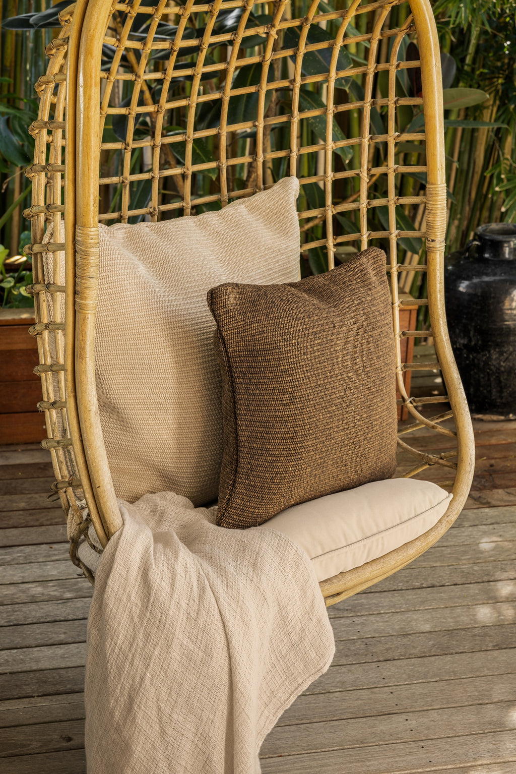 By Carmont Wren cushion cover in Topaz, close view on a hanging chair with a pale cushion and throw