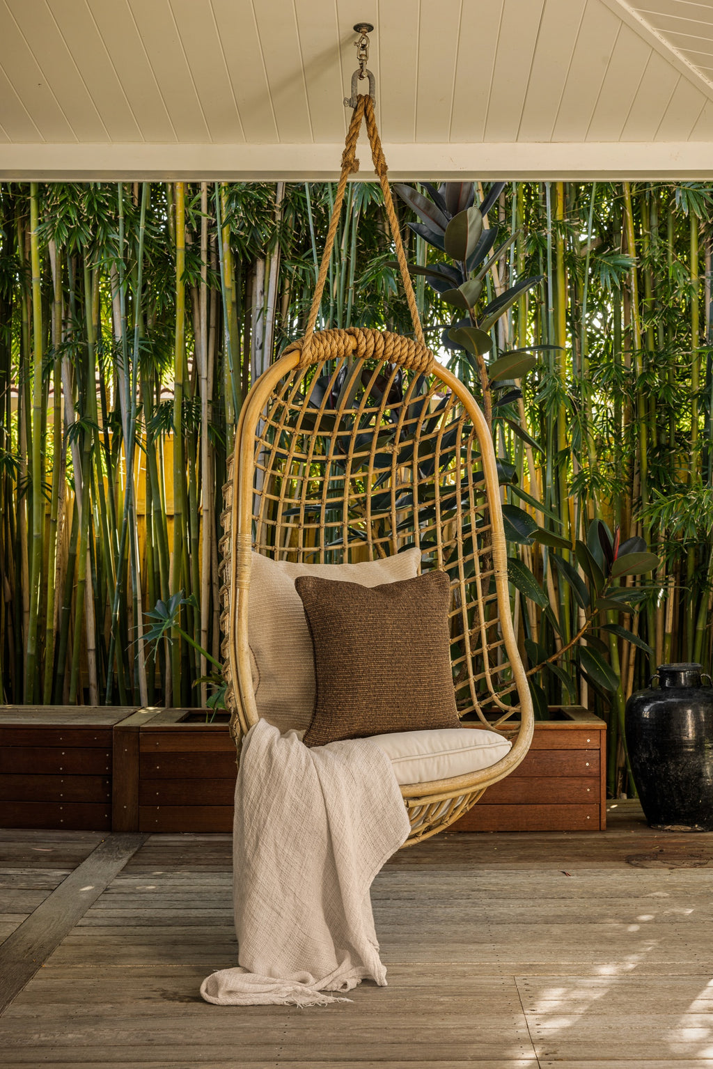 By Carmont Wren cushion cover in Topaz on a chair hanging from the ceiling of a covered deck