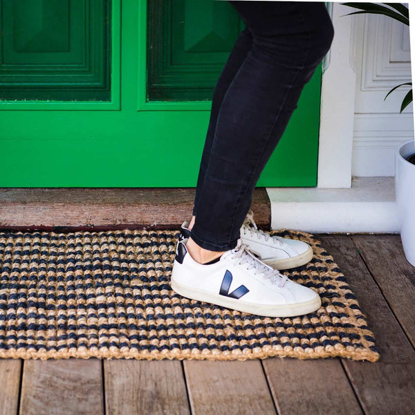 A person standing on a striped black and natural jute entrance mat. 