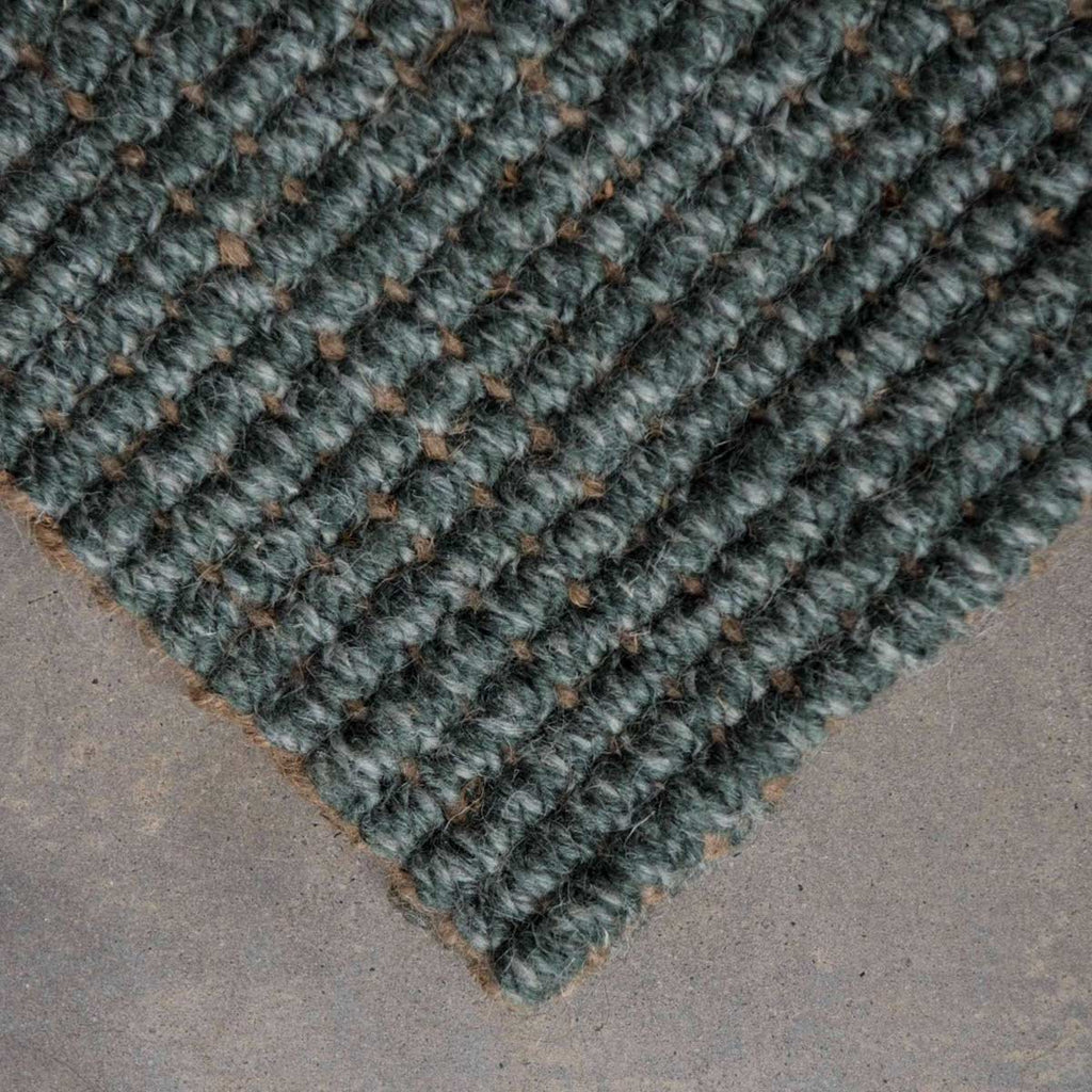 A close up of the corner of a muted forest green boucle weave wool and jute floor rug. 