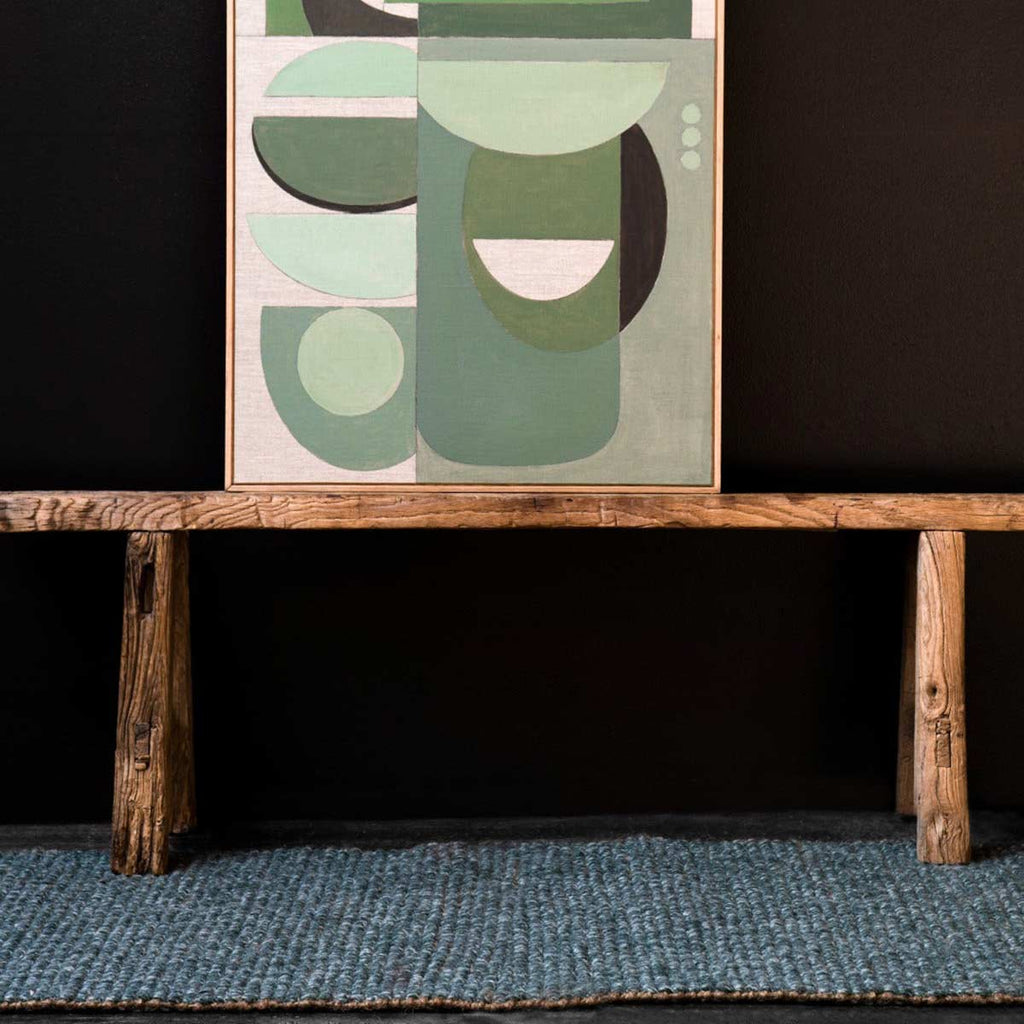 An end table sitting atop a floor runner made of wool and natural jute fibres, in a forest green tone. 