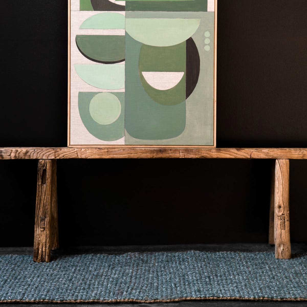 An end table sitting atop a floor runner made of wool and natural jute fibres, in a forest green tone. 